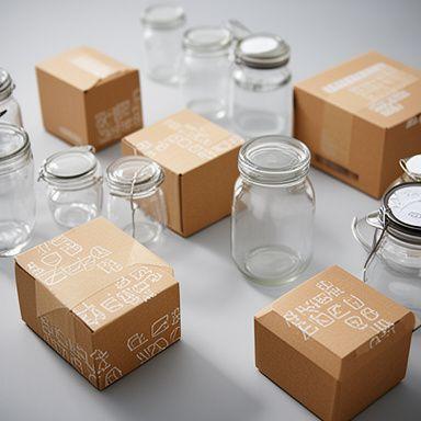Nachhaltige Versandkartons und Glasbehälter in einer sauberen Verpackungsstation mit natürlichen Schatten