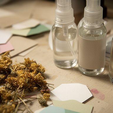 Handgefertigte Serumflaschen neben recycelten Papieretiketten und getrockneten Blüten auf einem Werkbanktisch